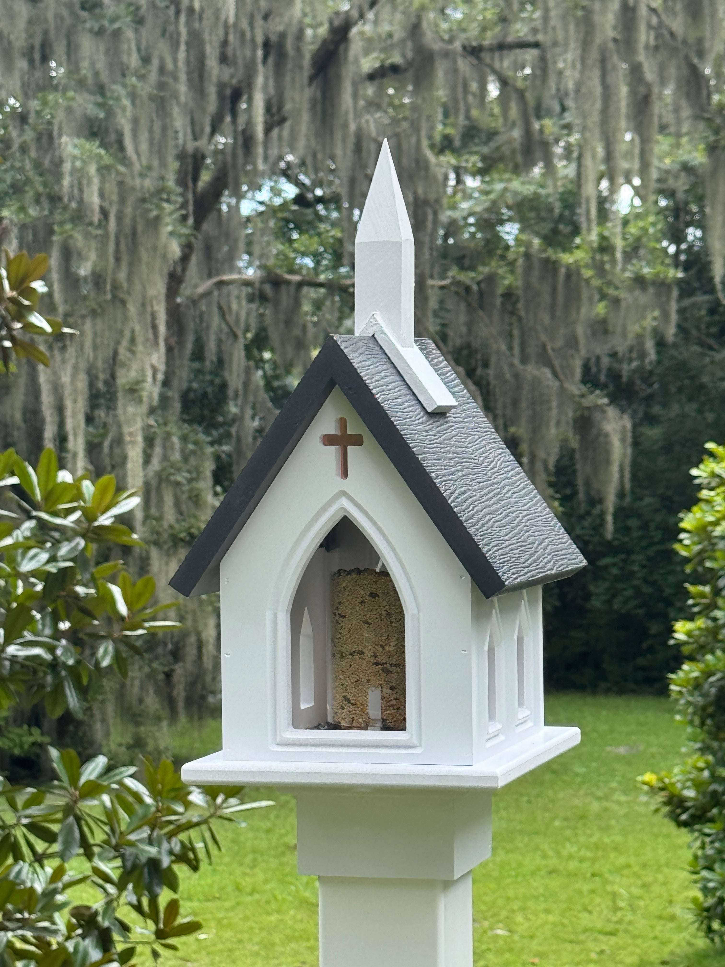 Decorative birdhouse shaped like a small church with a cross on a green lawn